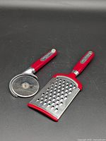 Cheese grater and pizza cutter side by side on black background