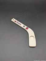 Full view of white plastic mini hockey stick bottle opener with Molson Canadian branding and integrated cap lifter