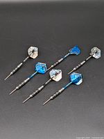 Five steel-tipped darts laid out on black surface showing points, barrels, shafts and flights