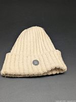 Cream ribbed knit beanie folded showing logo patch