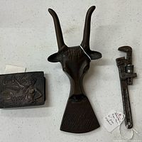 Three items laid out: antelope bottle opener, Coca-Cola box, pipe wrench