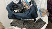 Duffle bag holding assorted O gauge track pieces, paint brushes in plastic sleeve, cork roadbed bag on table, extra switch and crossing track sections displayed