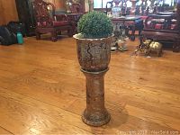 Full view of the ceramic jardiniere sitting on the painted pottery vase stand with plastic topiary ball inside.