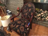 Front view of the large wooden armchair showing the rounded back and curved armrests, detailed with floral upholstery.