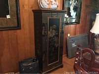 Full view of the black wood cabinet with Asian style hand-painted designs, placed against a wood paneled wall.