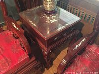 Top and side view of the hand carved wood side table showing mother of pearl inlay accents and glass top, surrounded by similar wood furniture with red cushion fabric.