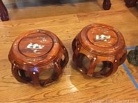 Pair of round, carved wooden stools with mother of pearl inlay decoration on top and open curved sides, shown on a wood floor