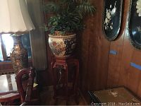 Full view of ceramic pot on wood stand with faux plant inside, showing overall size and environment.