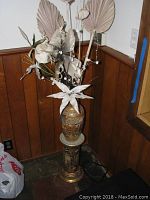 Full view of the oriental vase with faux flower arrangement on top and matching ceramic stand below against wood panel wall.