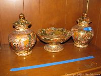 Overview of two Asian urns and a footed bowl placed on wooden shelf, showing the set and detailed color patterns