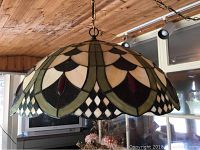 Close-up image of the Tiffany style stained glass hanging lamp with cream, green, black, and dark red glass pieces arranged in floral and geometric patterns.