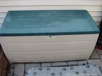 Full front view of the plastic deck box showing beige body and green lid with fading.