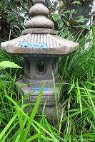 Front-side view of full cement pagoda in grass showing base, central body with oval openings, flared roof and top finial with blue tape labels