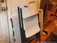 Photo showing stacked white plastic folding chairs with black metal frames against the wall near a door.