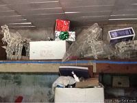 View of several lighted outdoor holiday decorations including reindeer and gift boxes stored on a high garage shelf.