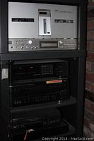 Metal shelving with multiple audio/video components: top Akai 77 deck, various black components including a VCR and cassette deck