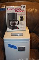 Overview photo showing boxed Hamilton Beach Aroma Express coffee maker on top of white ice maker with blue labeled dimensions.