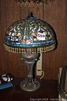Full view of lamp showing stained glass shade, bead fringe and metal base