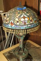 Full view of lamp showing multicolor stained glass shade with beaded fringe atop metal base