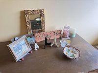 Lot overview on tabletop showing mirror, framed print, bowl, glass jar, candle holder, coaster and easels