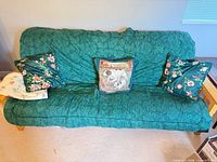 Full view of futon with green cover and three throw pillows