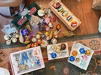 Overview of assorted boxed and loose ornaments on floor including train crate, boxed balls and icicles, loose balls, pinecones and angel