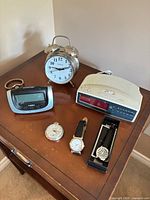 Lot overview on side table showing alarm clock, Timex digital clock, GE clock radio, pocket watch and two wristwatches