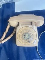 Front view of beige rotary phone with handset and dial visible