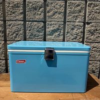 Full front view of light blue Coleman metal cooler showing logo, latch and overall condition