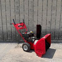 Full view of snowblower showing red housing, chute, tires, handle assembly