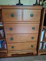 Front view of five-drawer wood dresser with green knobs and scalloped base