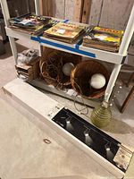Boxed track light on floor, two wicker pendants on shelf, green glass vessel adjacent