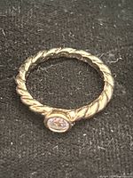 Front view of gold-tone twisted rope ring showing bezel-set clear stone
