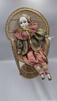 Full view of porcelain doll seated in wicker chair
