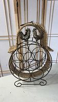 Front view showing wicker wrapped circular metal wine rack with rooster figures and scroll feet
