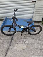 Left side view of black and blue 20-inch bicycle with kickstand and bottle cage