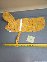 Raincoat exterior showing hood, strap, reflective strip, tape measure indicating length