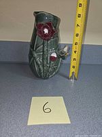 Front view of green ceramic vase with red lotus and frog, tape shows 7 in height