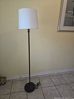 Full view of black floor lamp with white shade showing entire height and cord