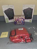 Overview of two LCD tablets in boxes, boxed karaoke machine, sealed red boxing gloves