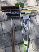 Lot overview showing two push brooms, green microfiber mop, four sponge mops
