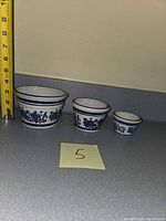 Three graduated blue and white ceramic pots next to ruler