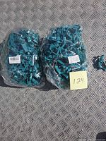 Two sealed bags of teal clips with barcode labels and sticky note showing lot number
