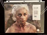 Full view of signed 8x10 photo inside sleeve with MaxSold tag and COA sticker