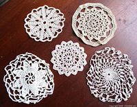 Five crochet doilies displayed on wooden surface