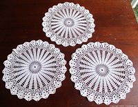 Three matching white round crochet doilies displayed on table
