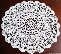 Full view of round white crochet doily on dark background
