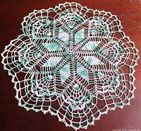 Full view of round green and white crocheted doily on wooden surface