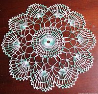 Full view of round green and white crochet doily on wooden surface