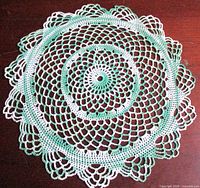 Full view of circular green and white crochet doily on table